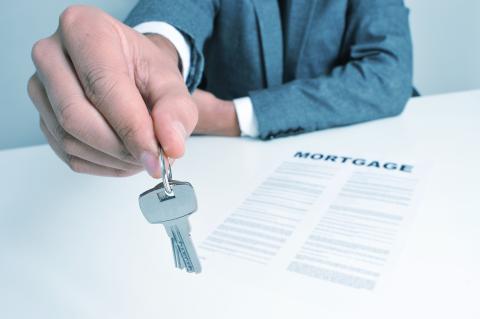 Man handing keys to person with a mortgage paper in front