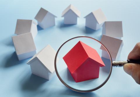 Person holding magnifying glass up to toy house